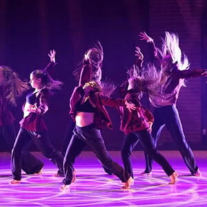 Groupe de danseurs en mouvement sur scène avec éclairage violet.
