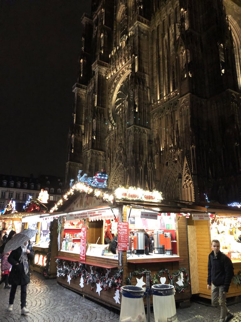Vue nocturne d'une cathédrale gothique illuminée avec marché de Noël en premier plan.