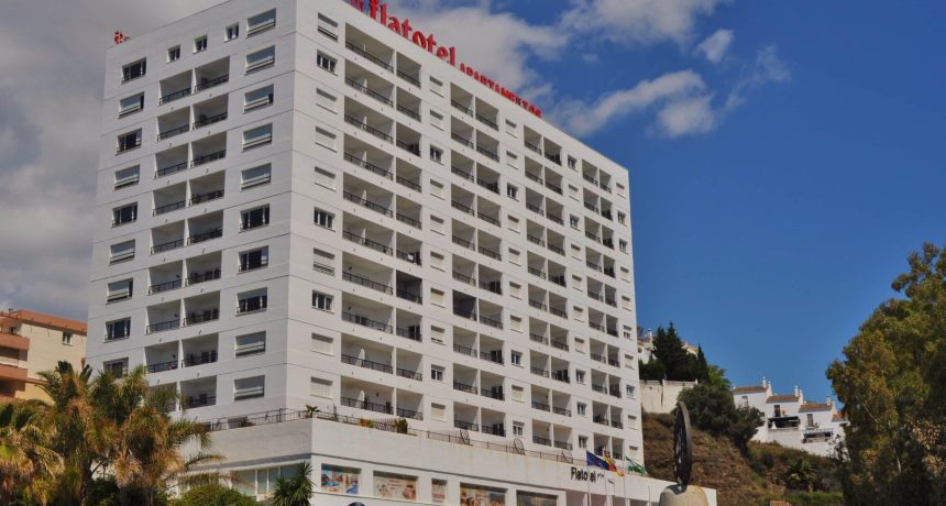 Hôtel moderne blanc avec plusieurs étages et balcons, vue sur le ciel bleu.