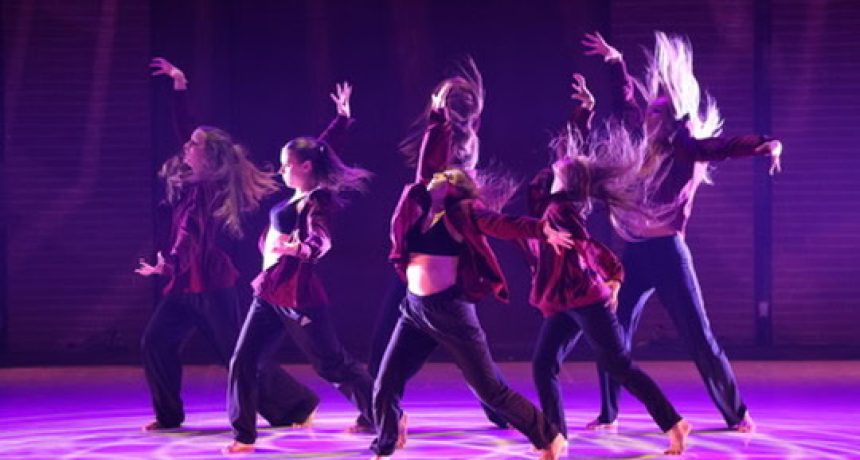 Groupe de danseurs en mouvement sur scène avec éclairage violet.