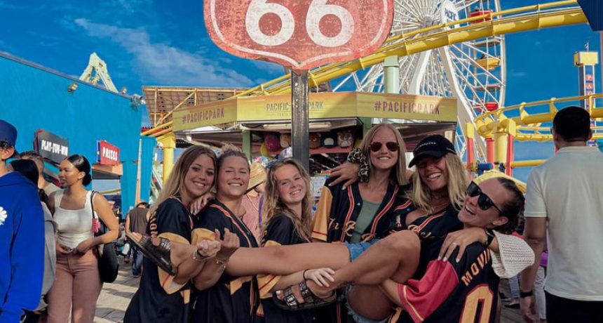Groupe d'amis souriants à la fête foraine Route 66 avec grande roue en arrière-plan.
