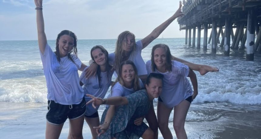Groupe d'amis souriants à la plage près de la jetée ensoleillée.