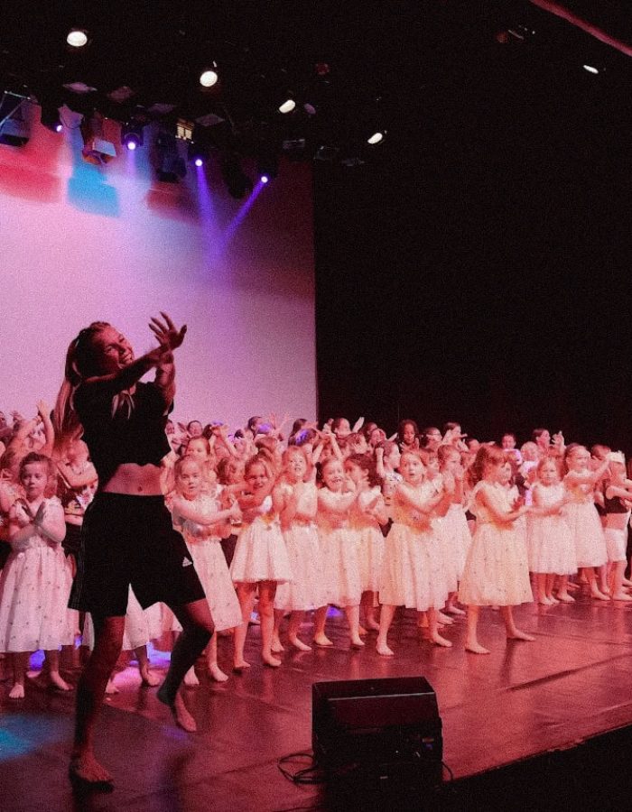 Ensemble d'enfants en costume blanc lors d'une performance de danse sur scène.