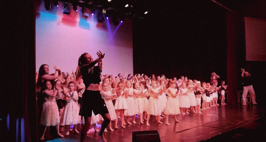 Ensemble d'enfants en costume blanc lors d'une performance de danse sur scène.