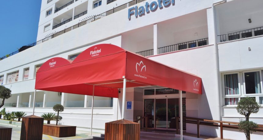 Entrée de l'hôtel Flotel avec un grand parasol rouge et un bâtiment moderne.